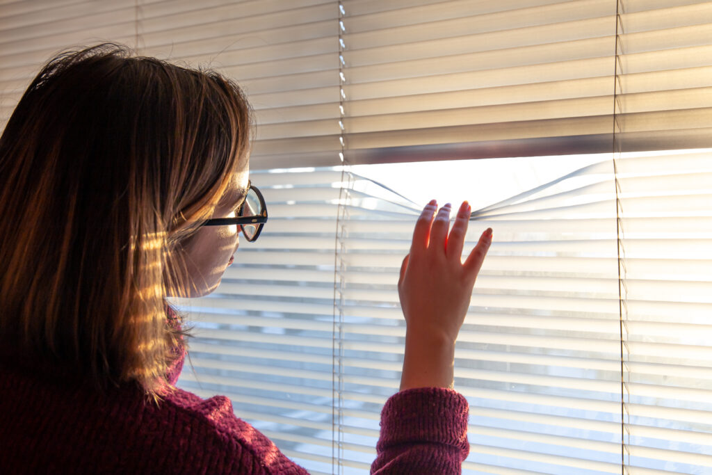 una mujer mira traves de las persianas la luz del sol de la manana 1
